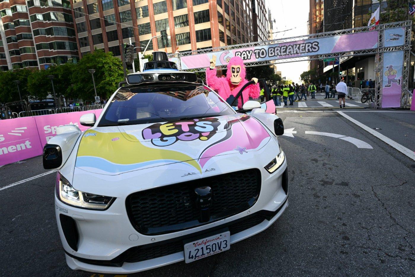 A pink gorilla beside a decorated pace car under the Bay to Breakers start arch on Howard Street