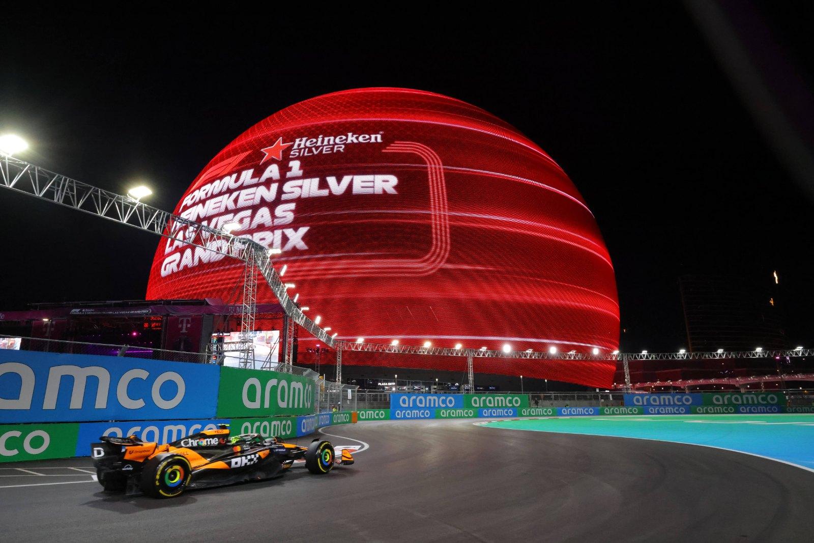 A Formula 1 car on the night circuit passing the Sphere lit red with Las Vegas Grand Prix branding