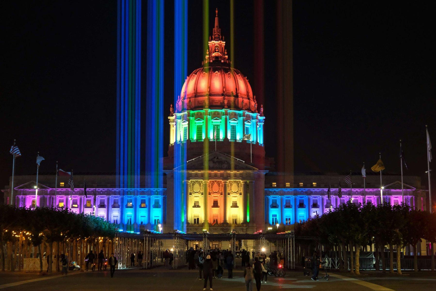 San Francisco City Hall lit in rainbow colors with light beams over Civic Center Plaza at night